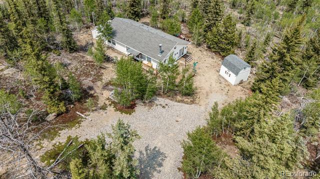 Aerial view of a house and detached shed beside a broad gravel driveway in a wooded setting.