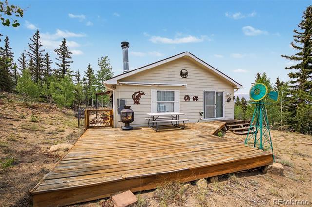 Small house with a broad wooden deck, picnic table, outdoor stove, and turquoise windmill.