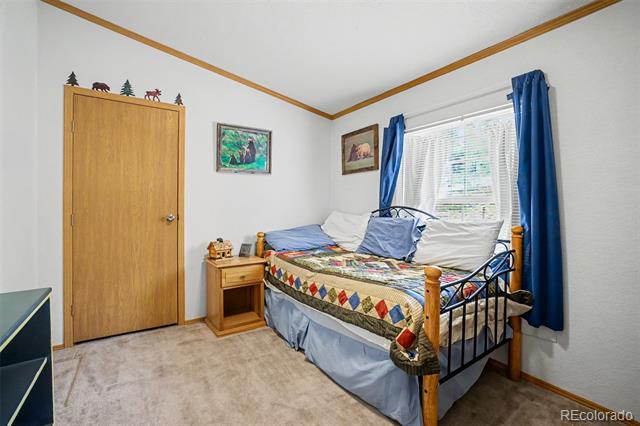 Bedroom with a metal-frame bed, colorful patchwork quilt, wooden nightstand, and blue curtains.