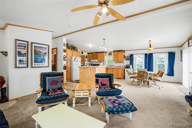 Open-plan living room and kitchen with blue chairs, wood cabinetry, and a dining area by blue-curtained windows.