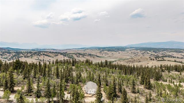 Aerial view of a house among evergreen trees, with rolling hills and distant mountains.