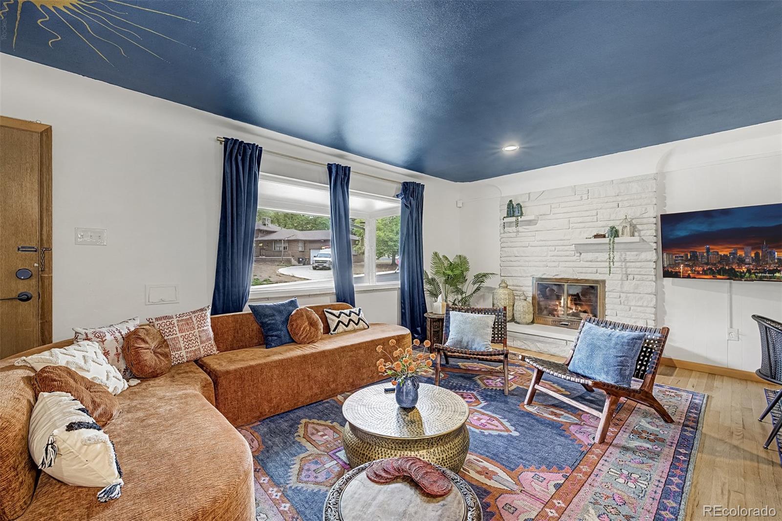 Living room with a white stone fireplace, tan sectional, colorful rug, and deep blue ceiling.