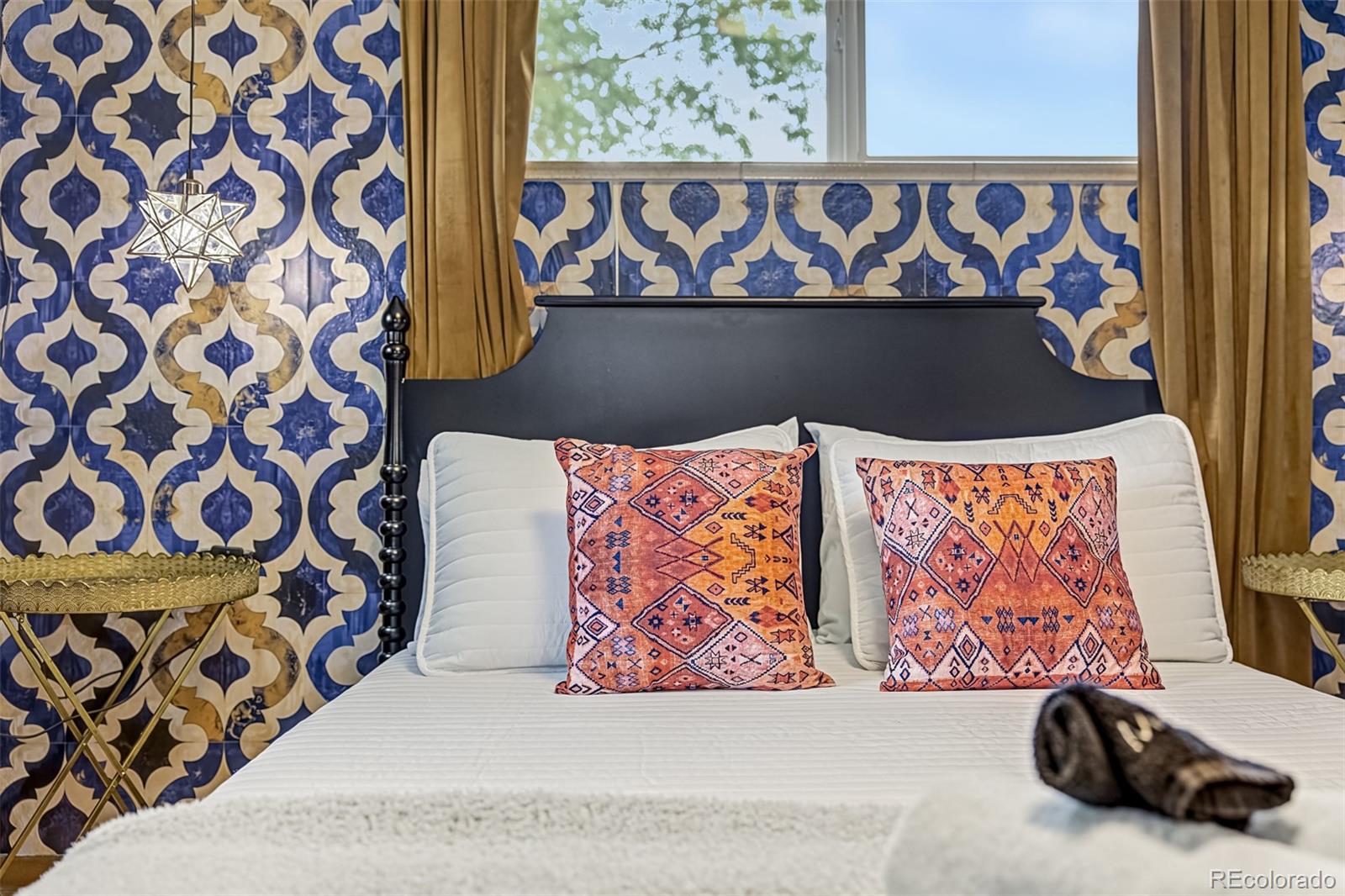 Bedroom with a white bed, coral patterned pillows, and a bold blue-and-cream tiled wall.