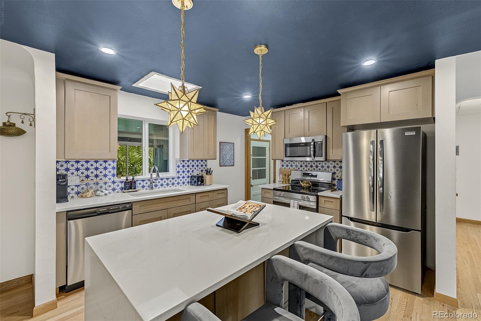 Kitchen with a white island, patterned blue tile backsplash, stainless steel appliances, and gold star pendant lights.