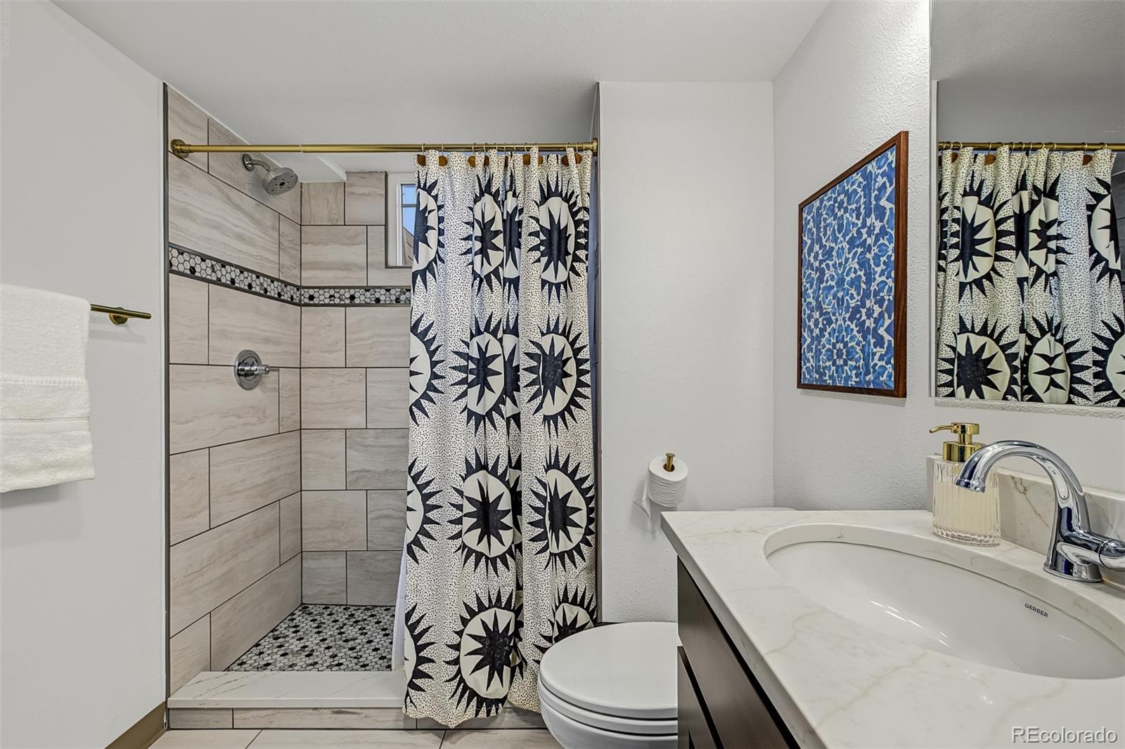 Bathroom with a tiled walk-in shower, patterned curtain, and marble-look vanity.