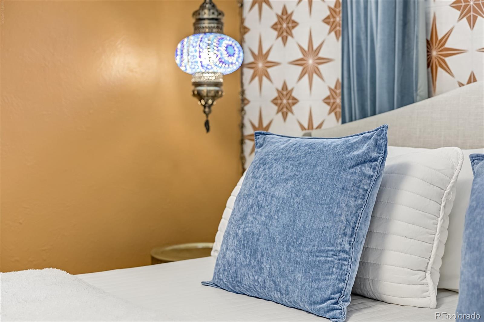 Bedroom with blue pillows, a patterned accent wall, and a decorative hanging lamp.