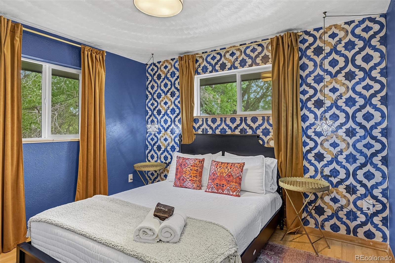 Staged bedroom with a white bed, bold blue patterned accent wall, and mustard curtains.