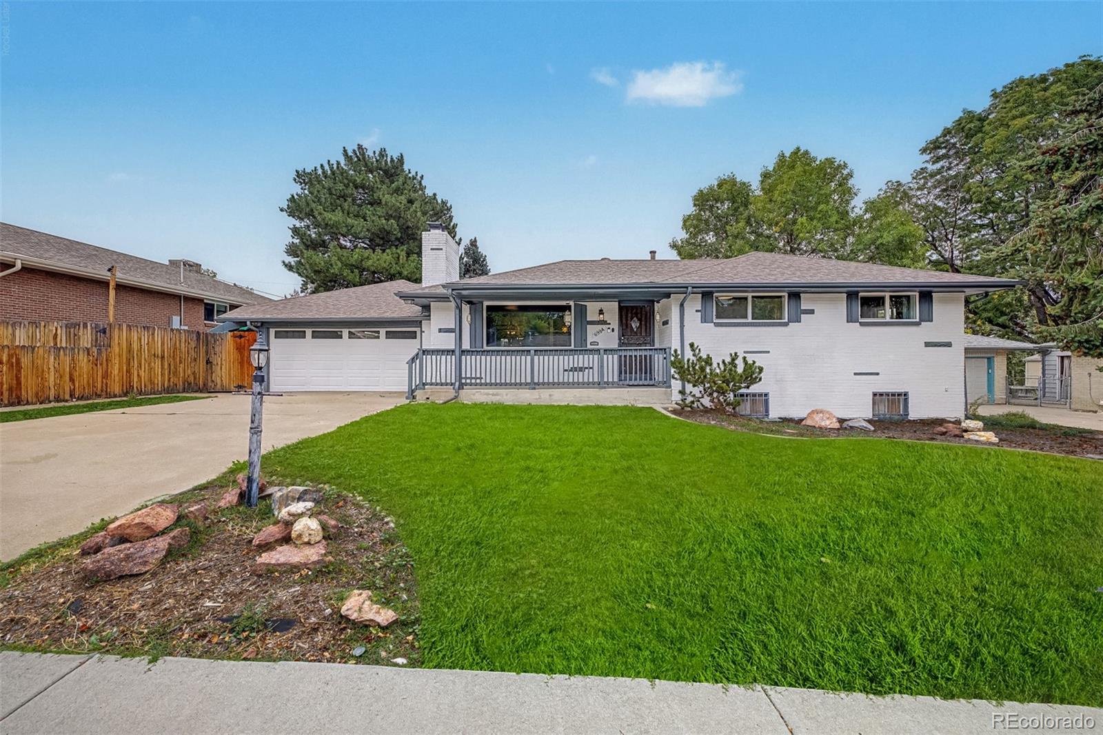 White brick ranch house with a covered porch, attached garage, and broad green front lawn.