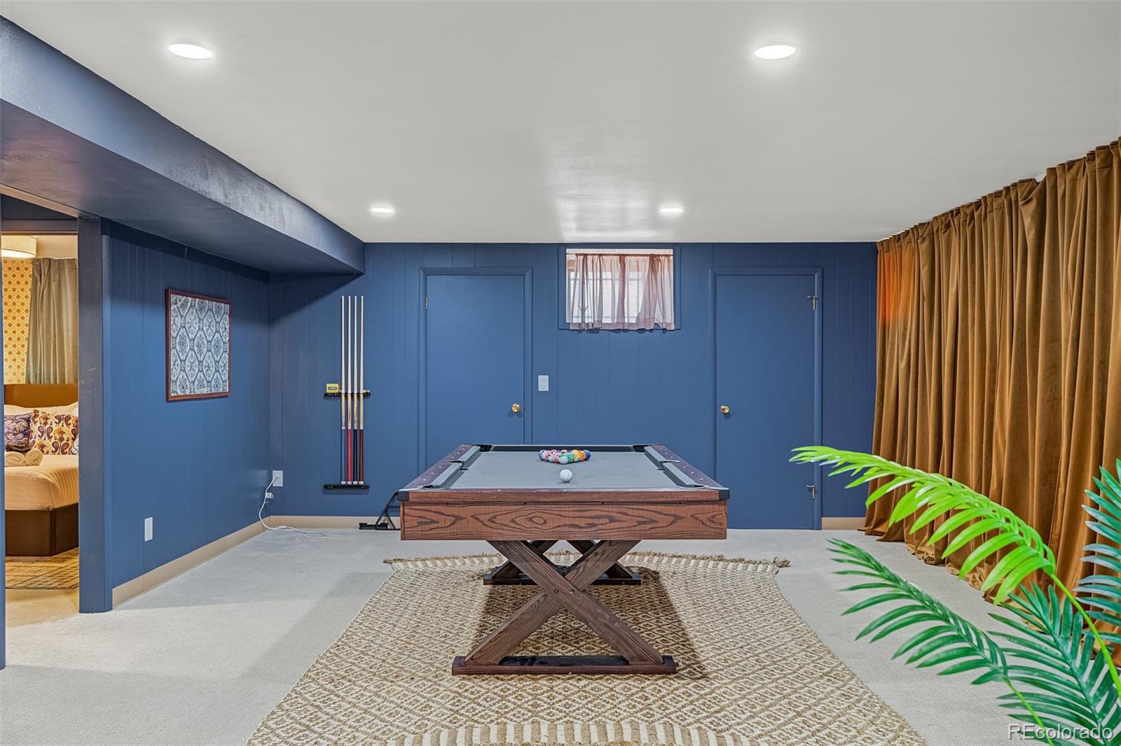 Basement game room with a pool table, blue paneled walls, and brown curtains.