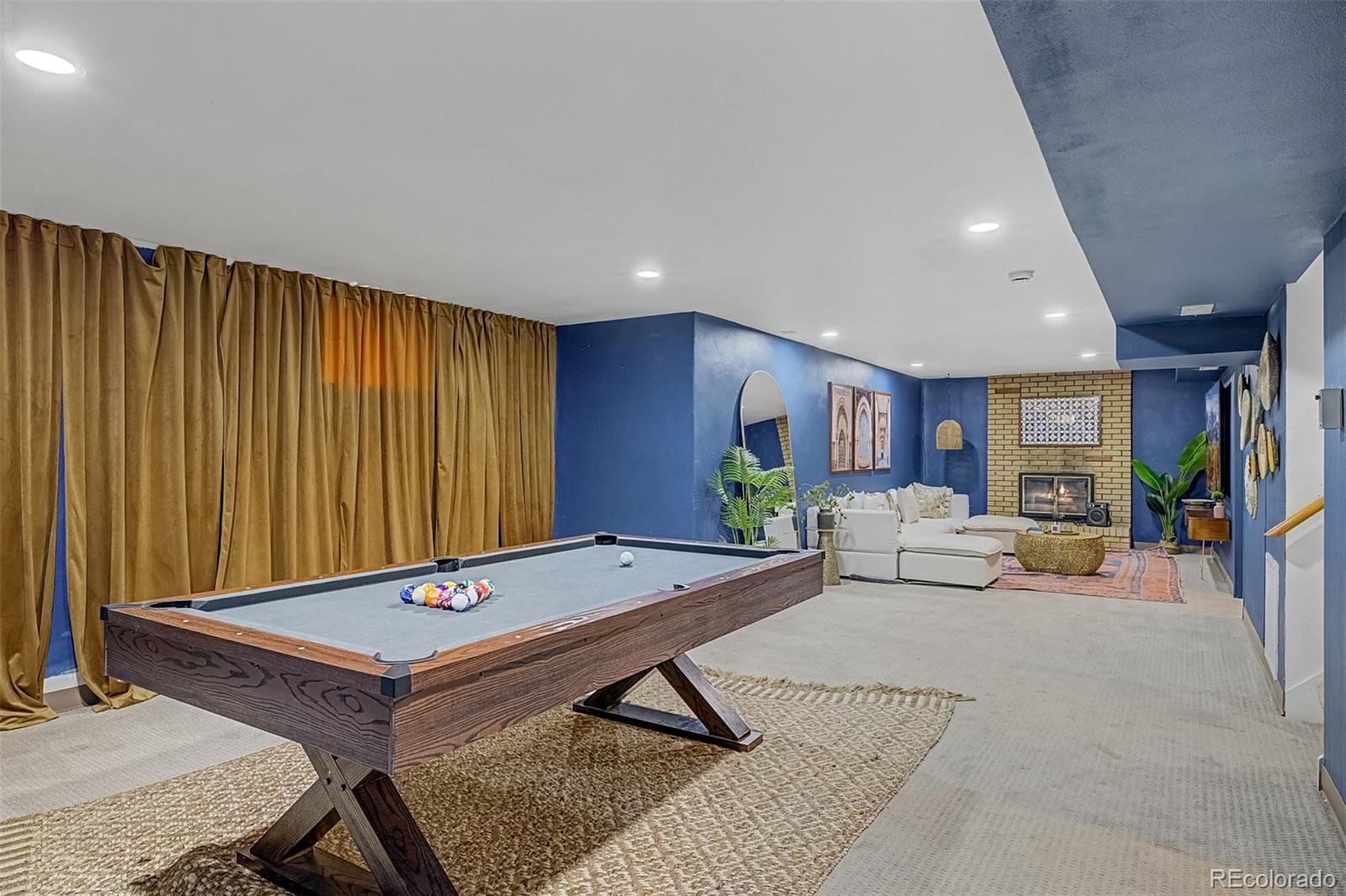 Basement recreation room with a pool table and a lounge area centered on a brick fireplace.