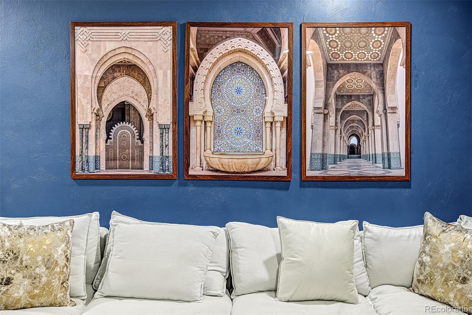 Living room with a white sectional sofa beneath three framed architectural photographs on a blue wall.