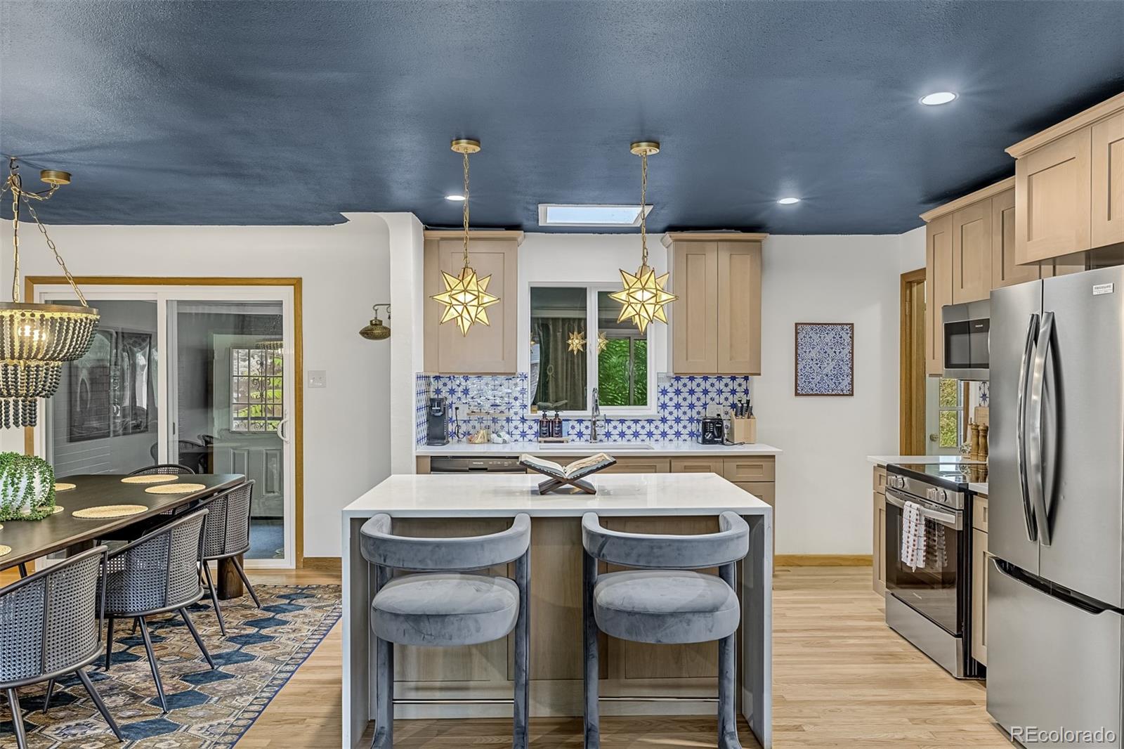 Kitchen with a large white island, blue patterned backsplash, dark blue ceiling, and adjoining dining area.