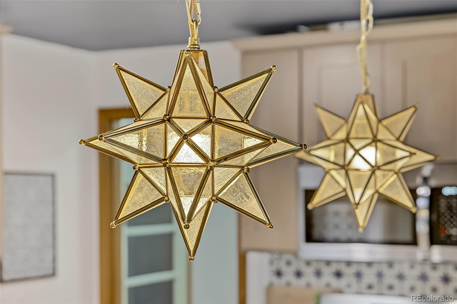 Gold geometric star pendant lights hang above a kitchen with a patterned tile backsplash.