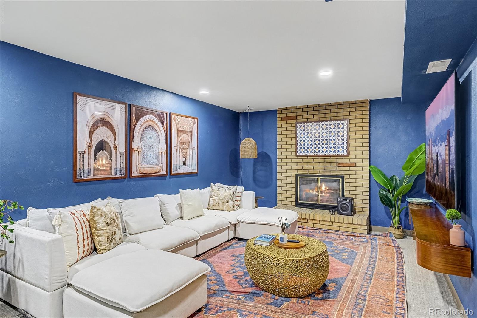 Living room with blue walls, a white sectional, patterned rug, and brick fireplace