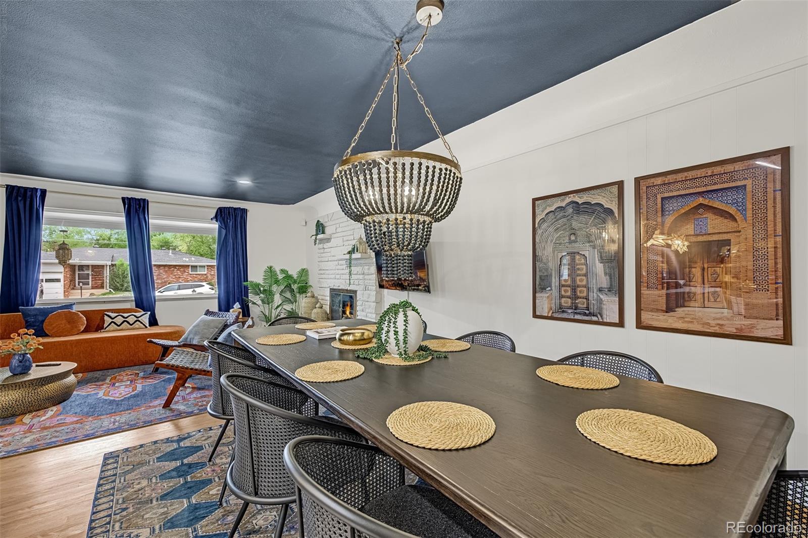 Dining and living area with a beaded chandelier, blue ceiling, and white brick fireplace.