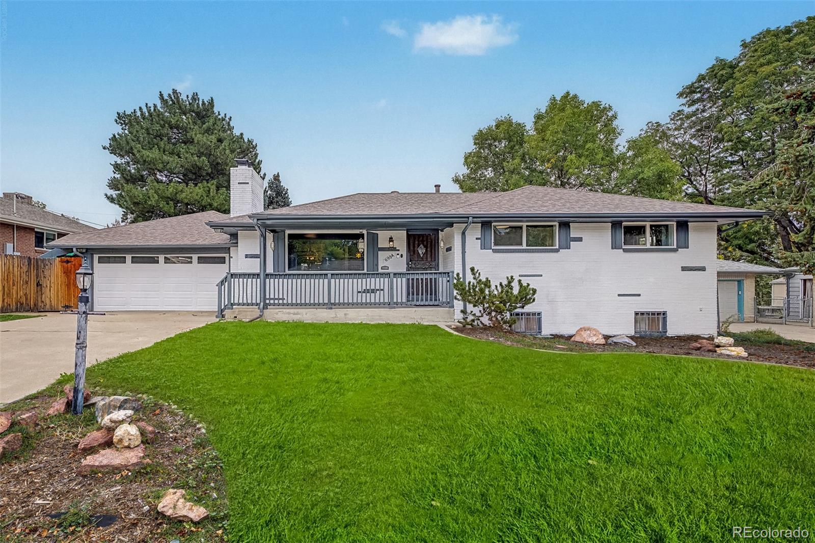 Single-story white brick home with an attached garage, covered porch, and broad green lawn.