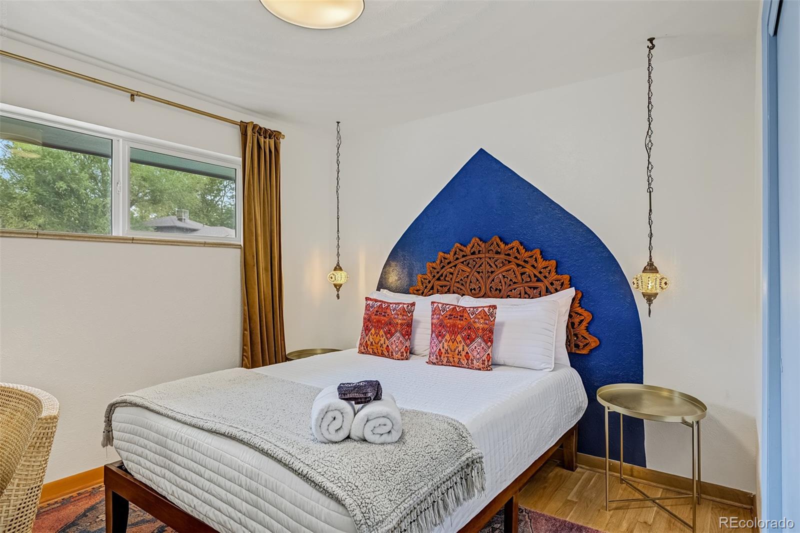 Furnished bedroom with a blue accent wall, carved headboard, and pendant lights.