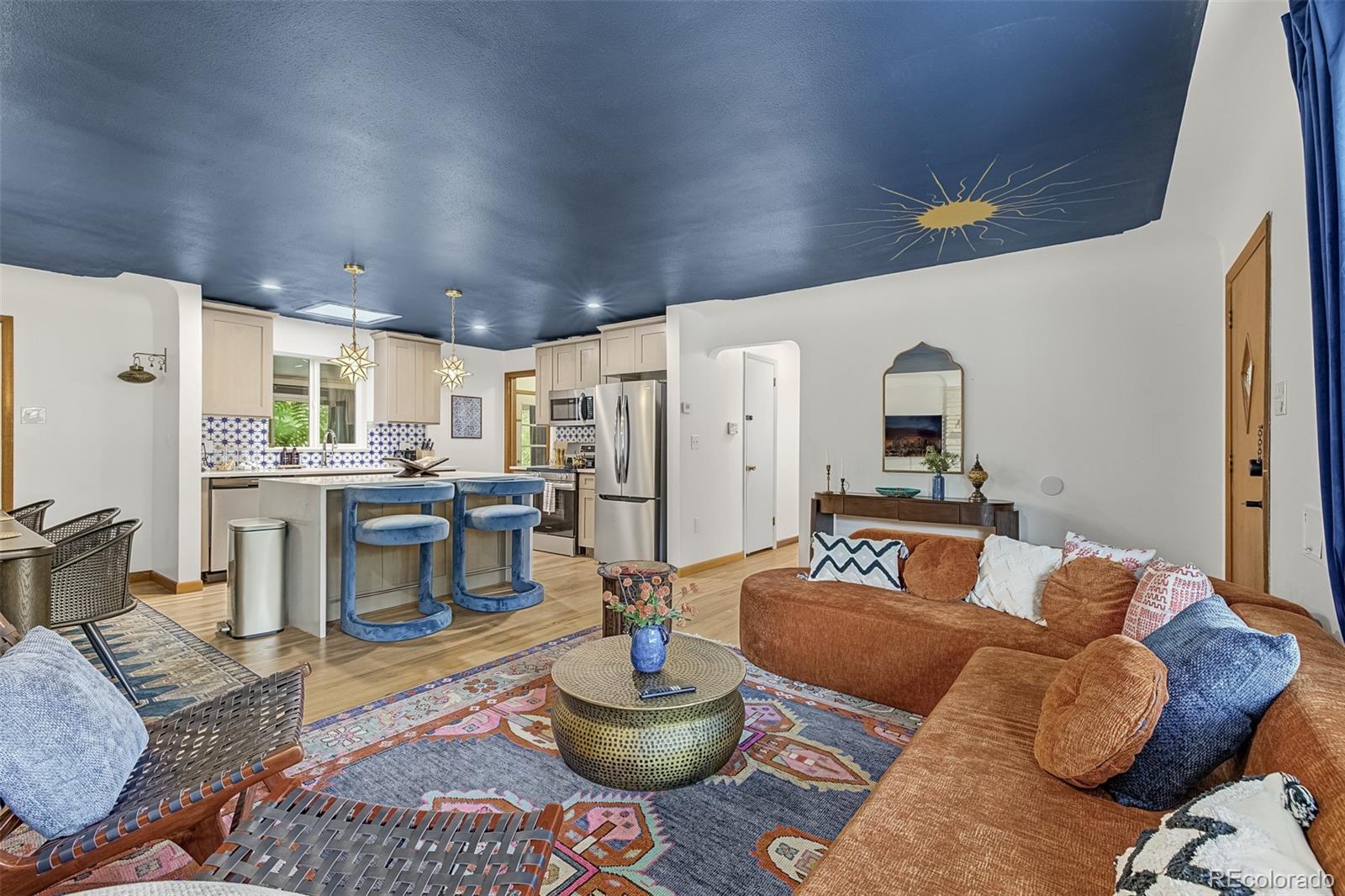 Open-plan living room and kitchen with a blue ceiling, patterned backsplash, and rust-colored sectional.