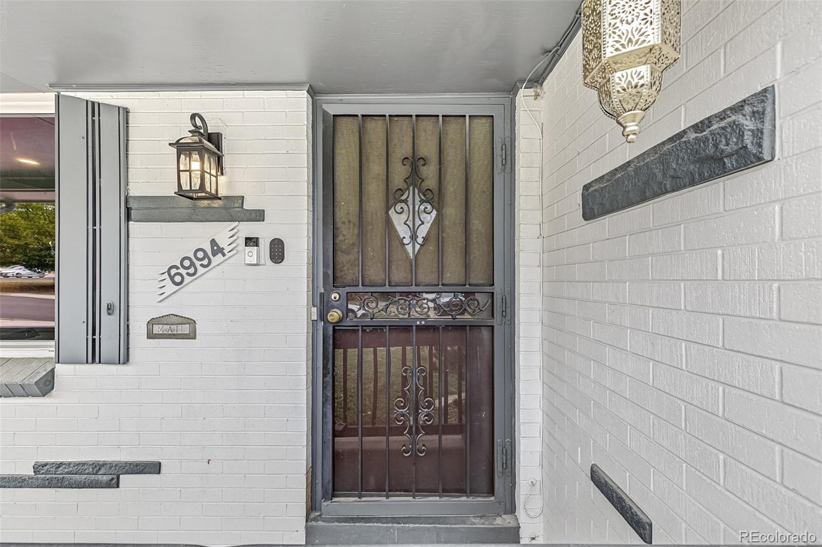 Front entry with a decorative black metal security door and 6994 address plaque on white brick.