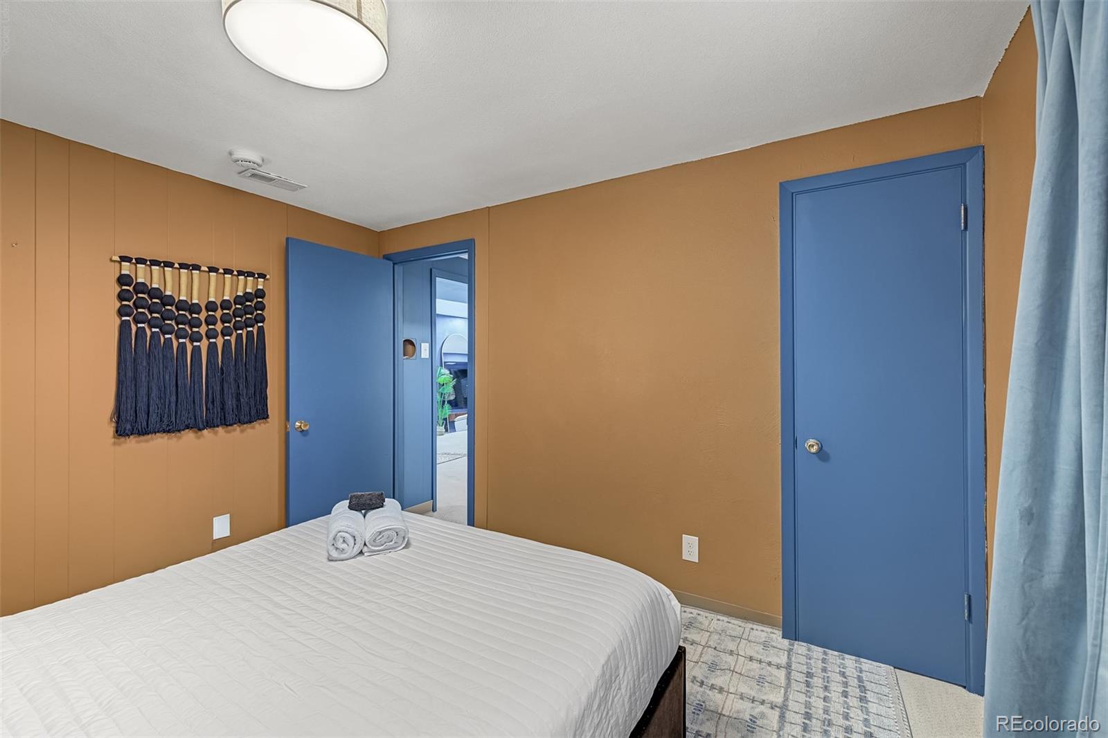 Bedroom with a white bed, tan walls, blue doors, and a patterned rug.