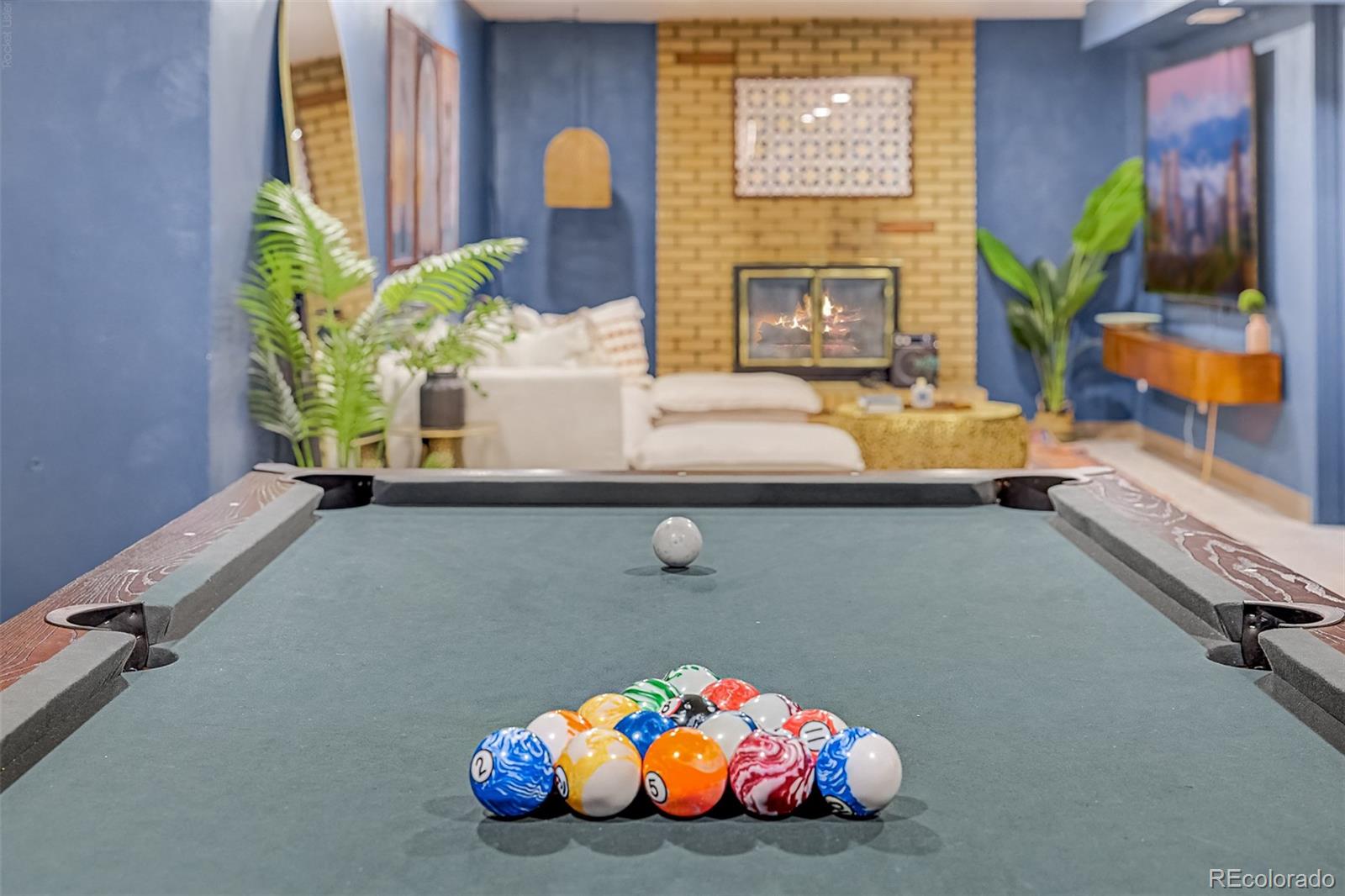 Game room with a pool table, racked balls, white seating, and a lit brick fireplace.