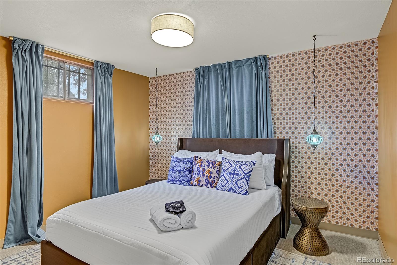 Staged bedroom with a large bed, patterned accent wall, and blue curtains.