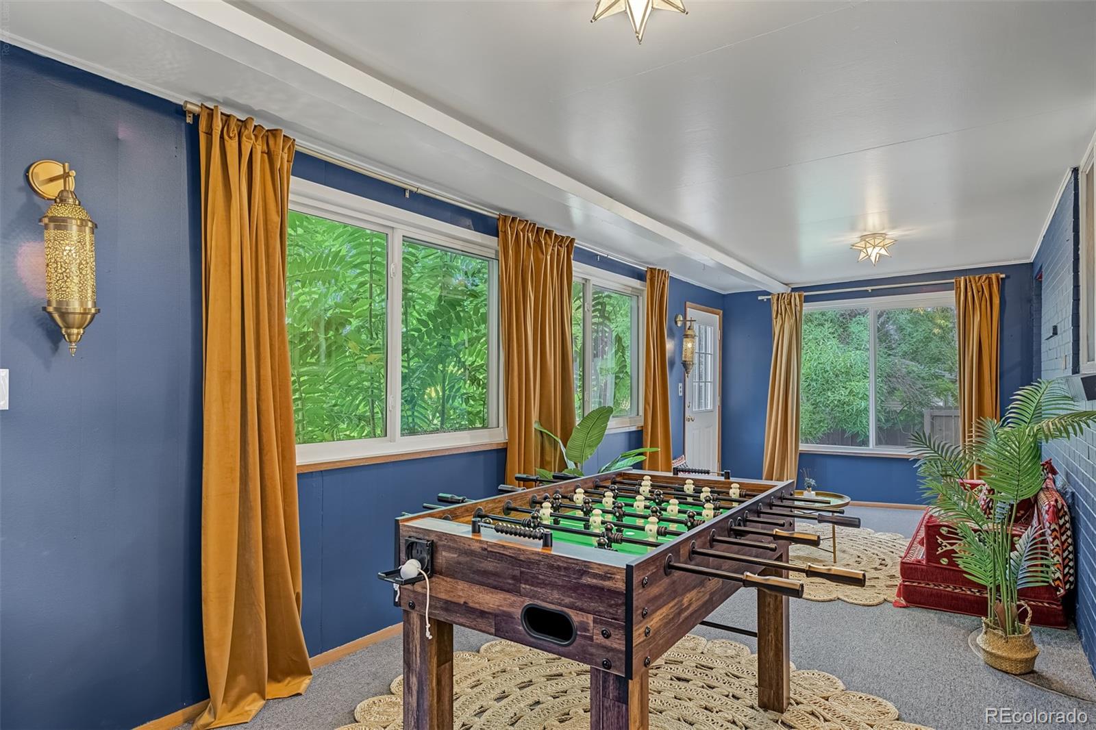 Furnished game room with a foosball table, blue walls, and large windows framed by mustard curtains.