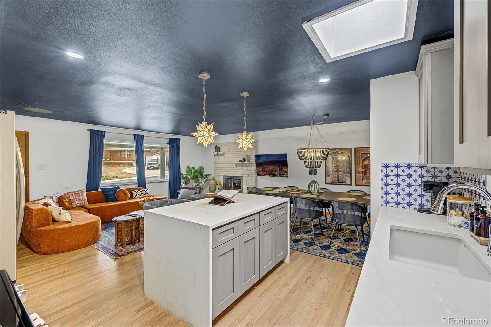 Open-plan kitchen with a large white island, blue-and-white backsplash, and adjoining orange-sofa living area.