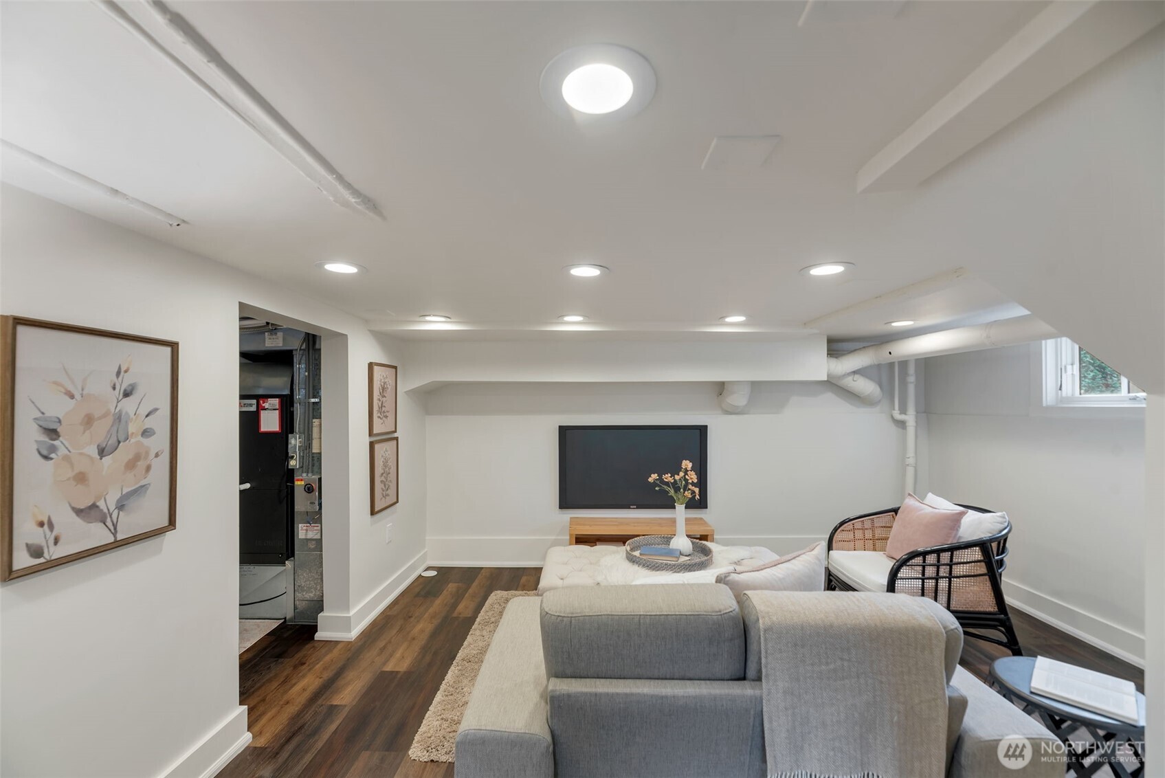 Furnished lower-level living room with a gray sectional, wall-mounted television, and dark wood flooring.