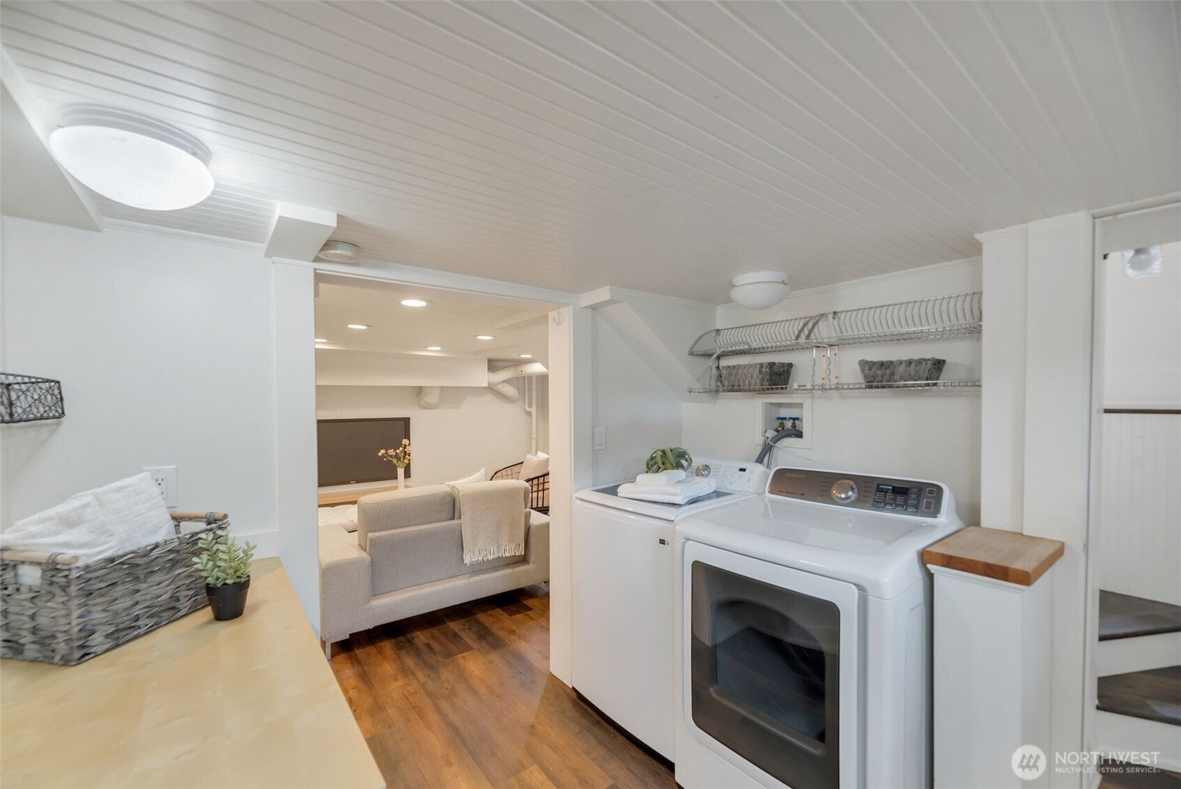 Laundry room with washer and dryer, wire shelving, and an adjoining sitting area.