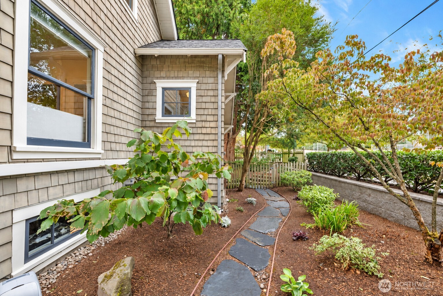 Shingle-sided home beside a landscaped courtyard with a curved stepping-stone path and mature trees.