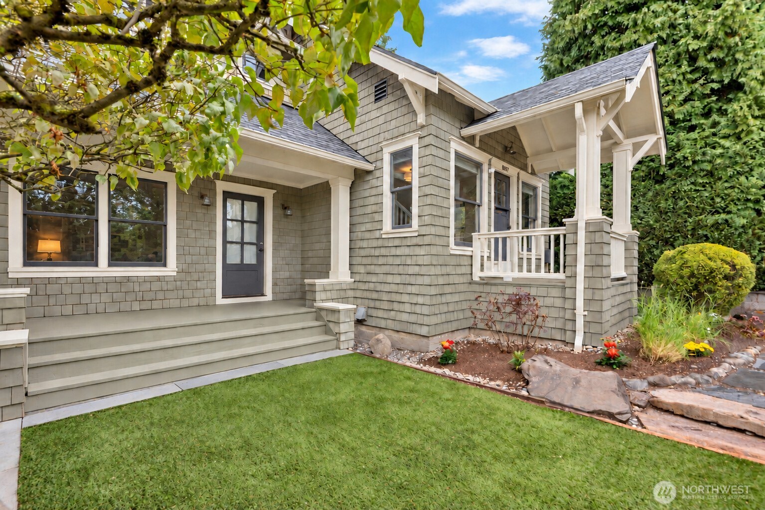 Gray shingle-sided home with a covered porch, broad front steps, and landscaped front garden.