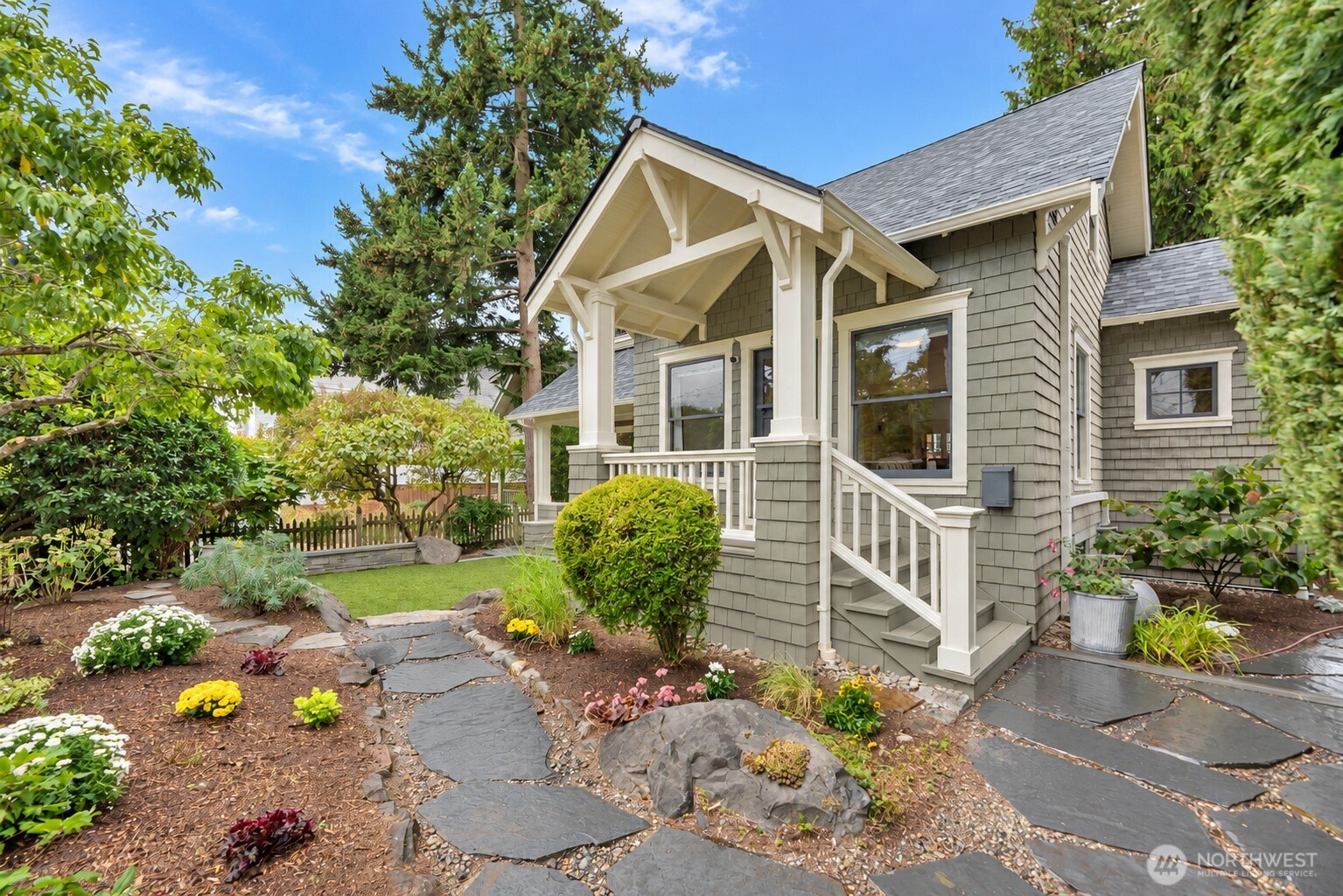 Gray shingle-sided house with a covered porch, white trim, and a landscaped stone walkway.