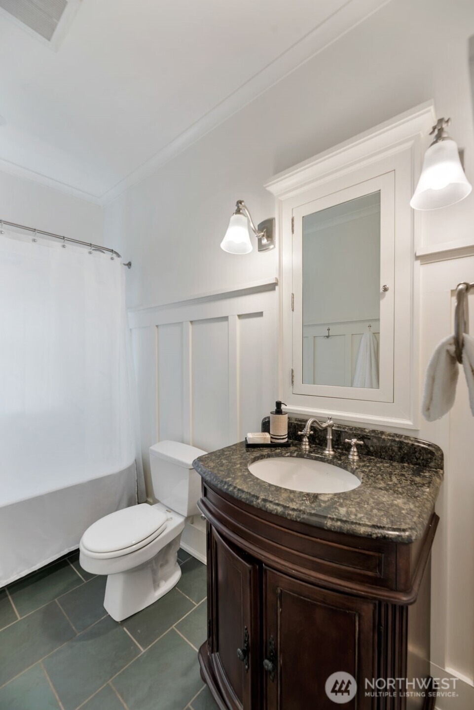 Bathroom with a dark wood vanity, granite counter, mirrored cabinet, and white tub and shower curtain.