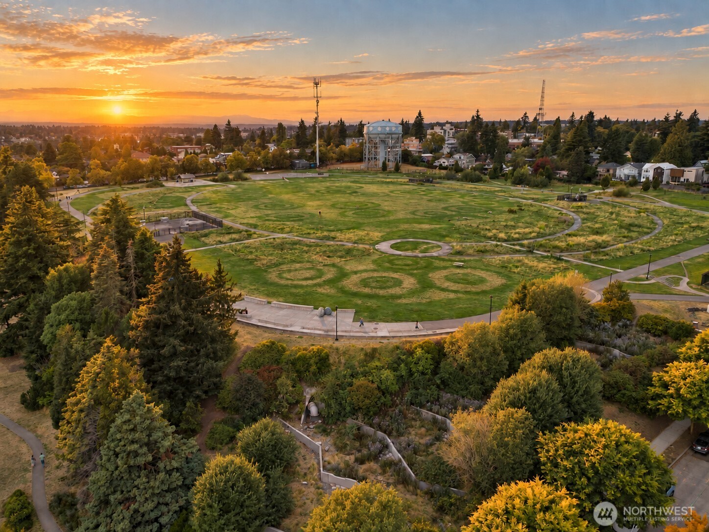 Aerial view of a landscaped neighborhood park with winding paths and a water tower at sunset.