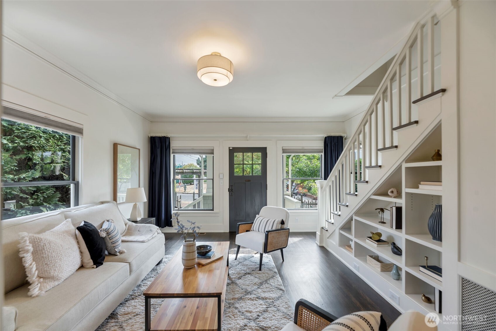 Staged living room with a white sofa and built-in shelving beneath the staircase.