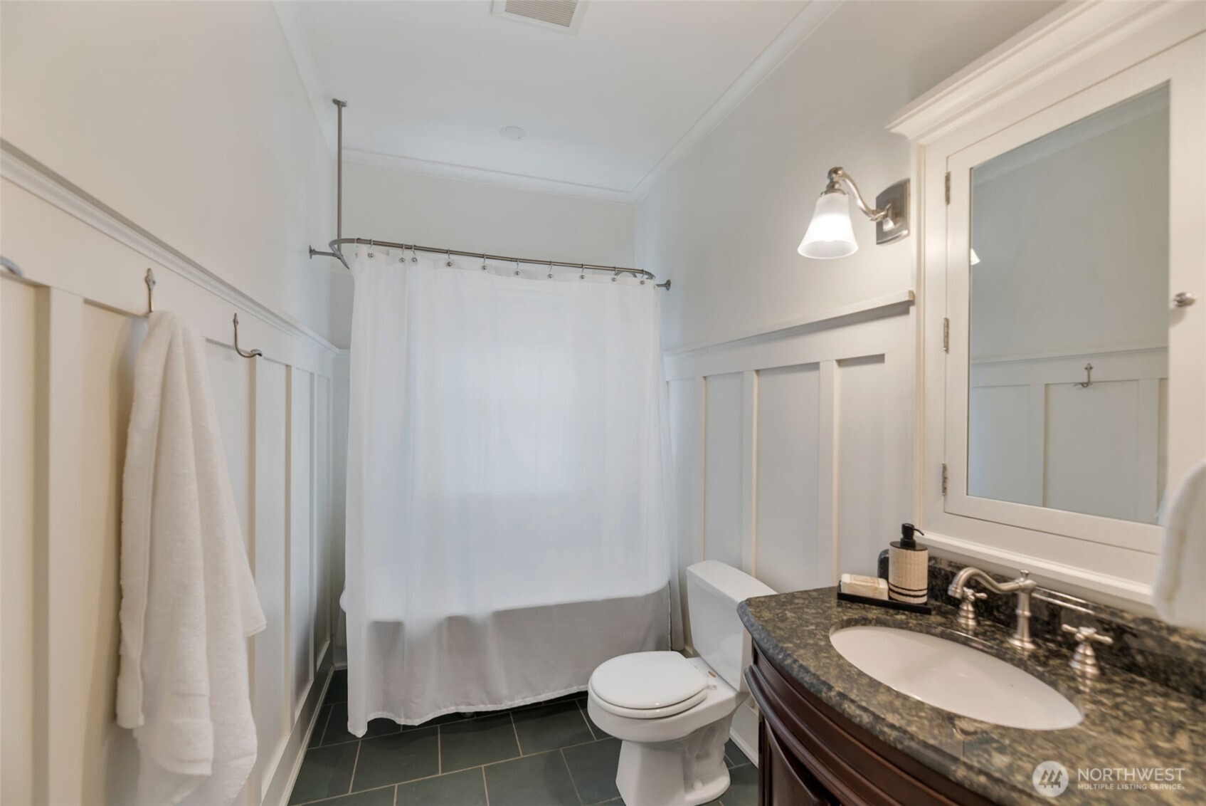 Bathroom with white paneled wainscoting, a curtained shower, and a dark stone vanity.