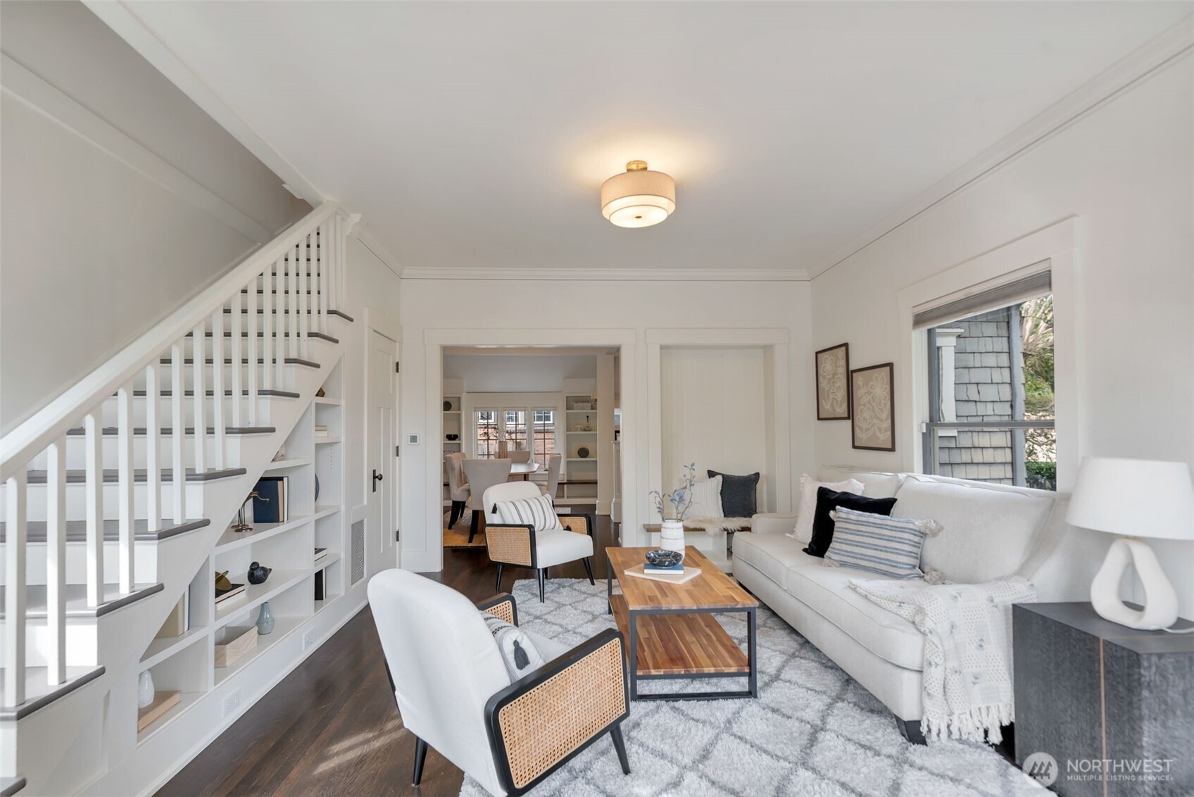Staged living room with built-in stair shelving, white seating, and a view into the dining room.