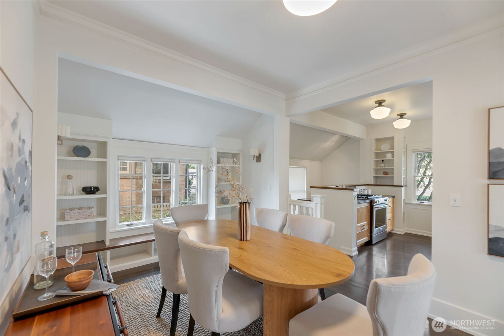 Dining room with an oval wood table and upholstered chairs, opening to a bright kitchen.