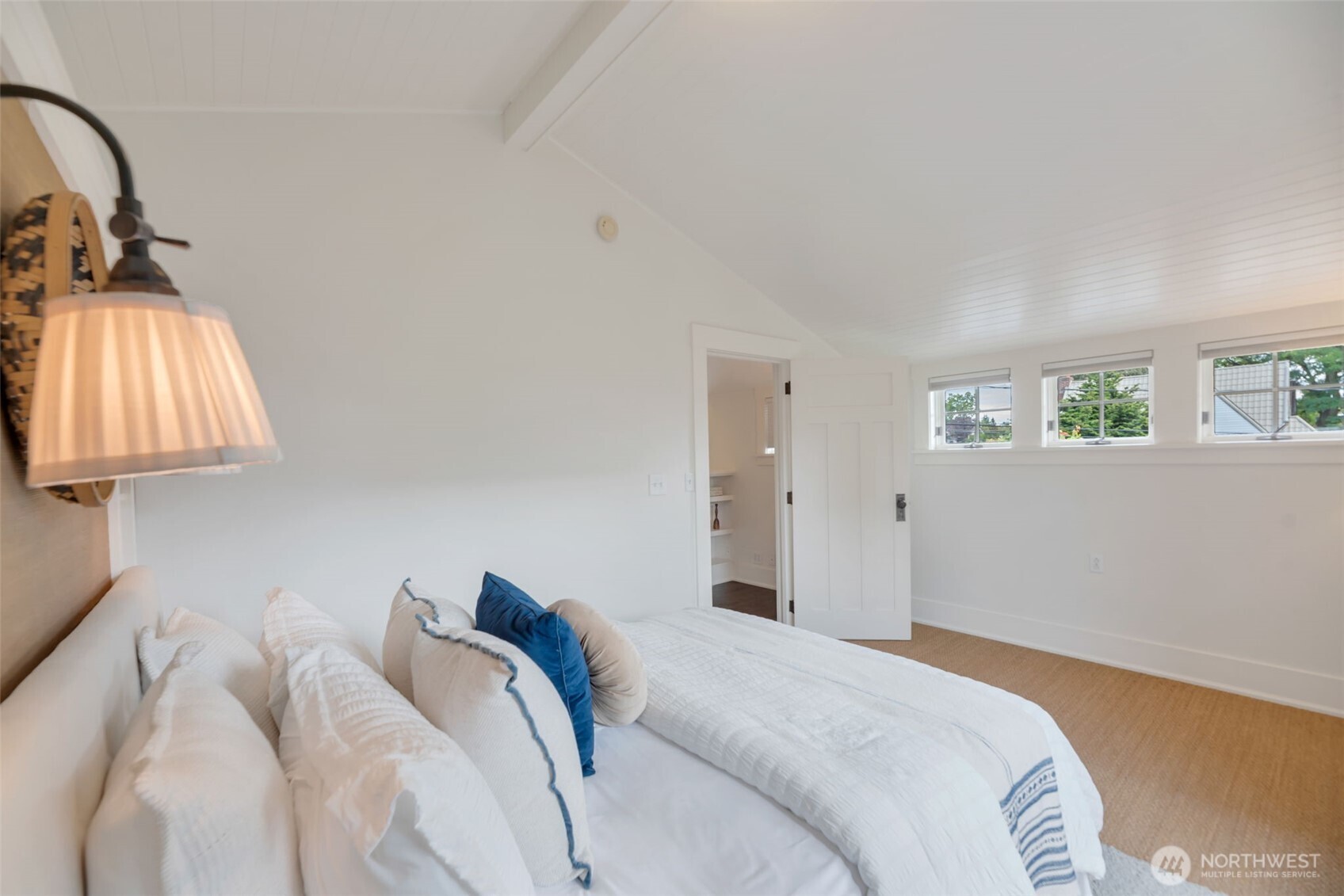 Furnished bedroom with a white bed, sloped beadboard ceiling, and high windows.