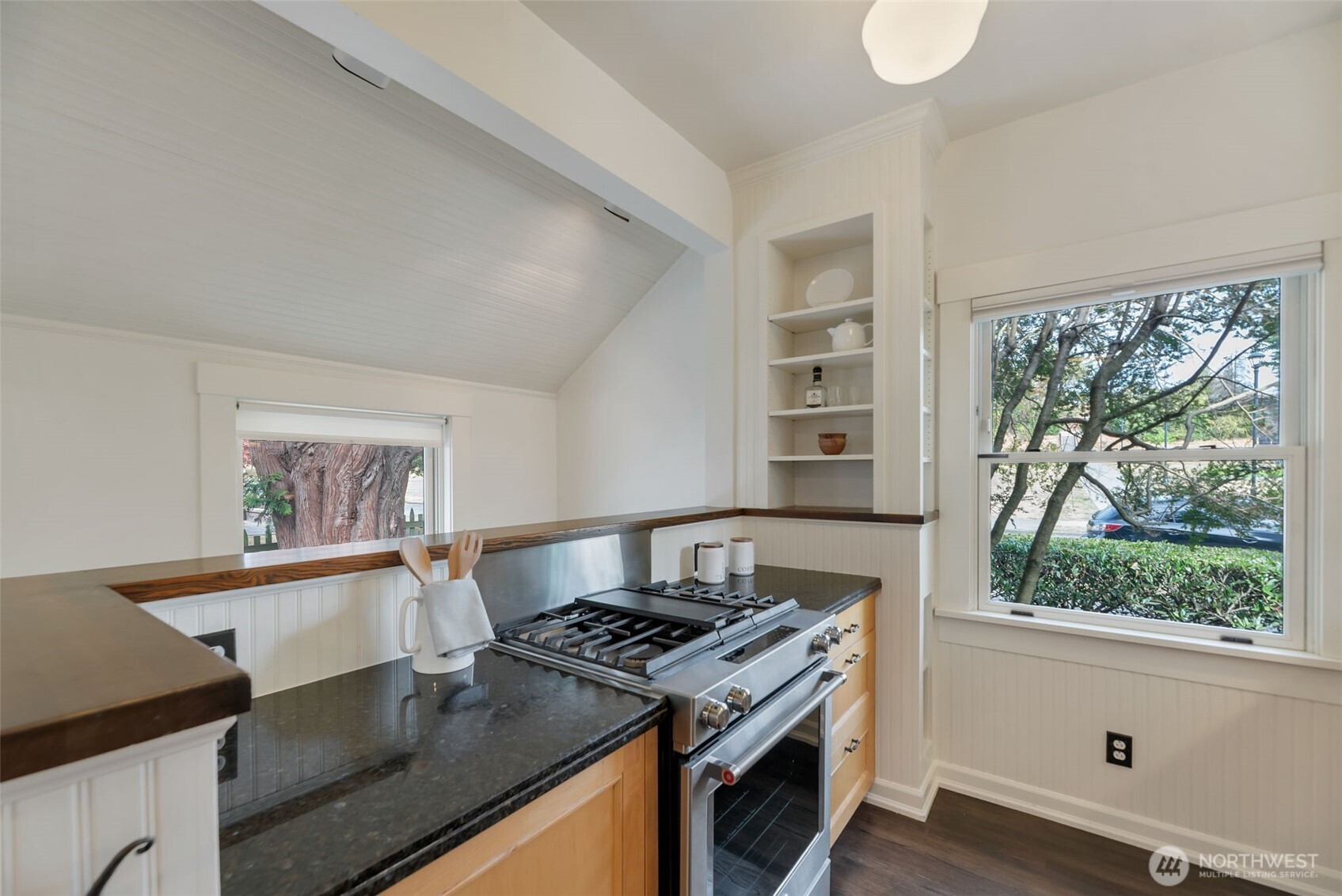 Kitchen with a vaulted ceiling, dark counters, stainless-steel range, and tree views through the windows.