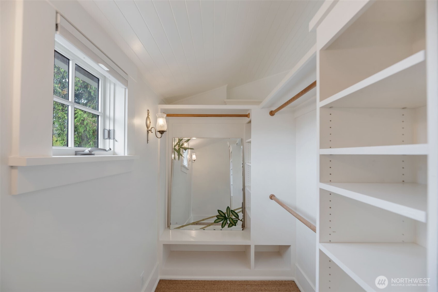 Walk-in closet with white built-in shelves, wooden hanging rods, and a large mirror above a bench.