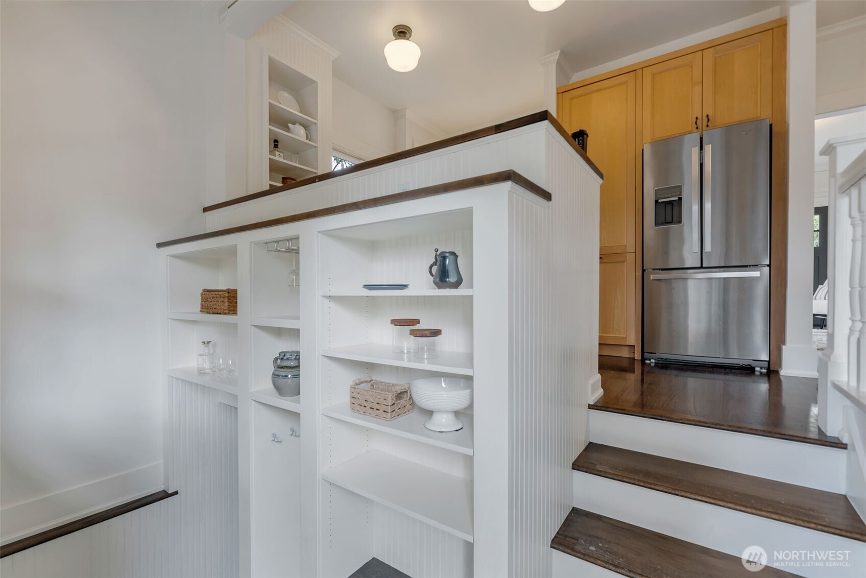 Kitchen with built-in white display shelves, wood cabinets, stainless steel refrigerator, and dark wood steps.