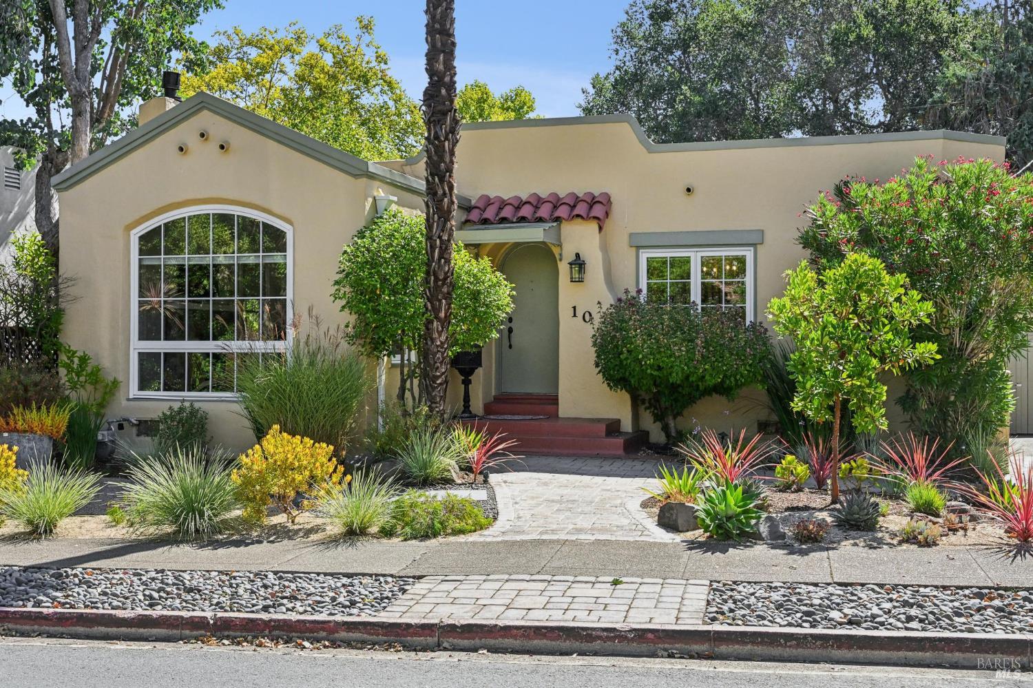 Cream stucco home with an arched window, red tile entry awning, and landscaped front garden.