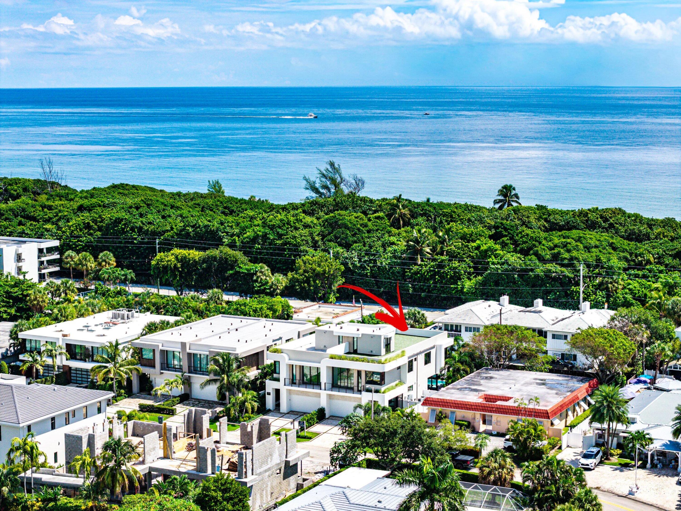 Aerial view of the arrow-marked modern home, with the ocean beyond the surrounding houses and trees.
