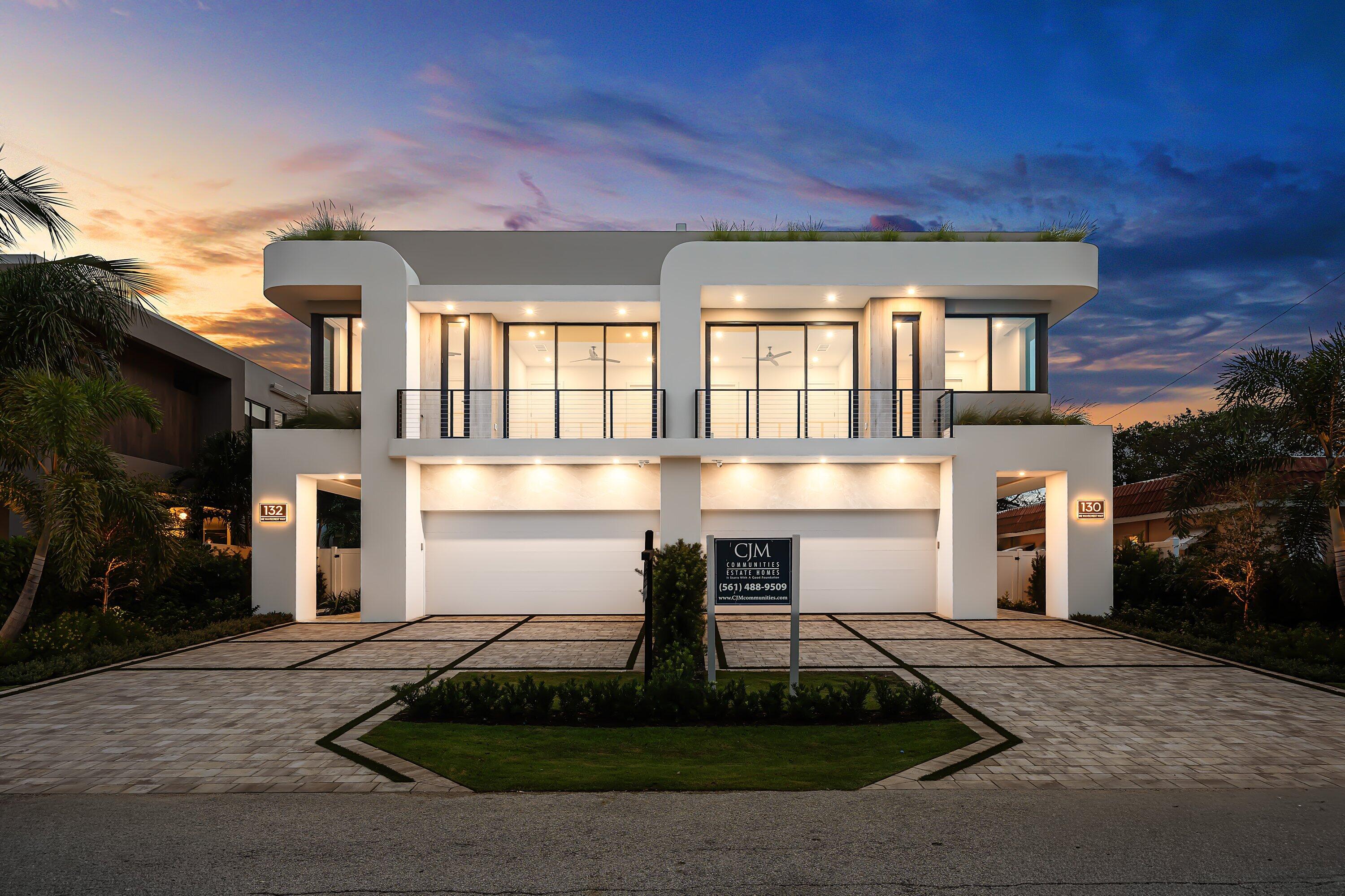 Modern white two-story home with a wide balcony and illuminated windows at dusk.