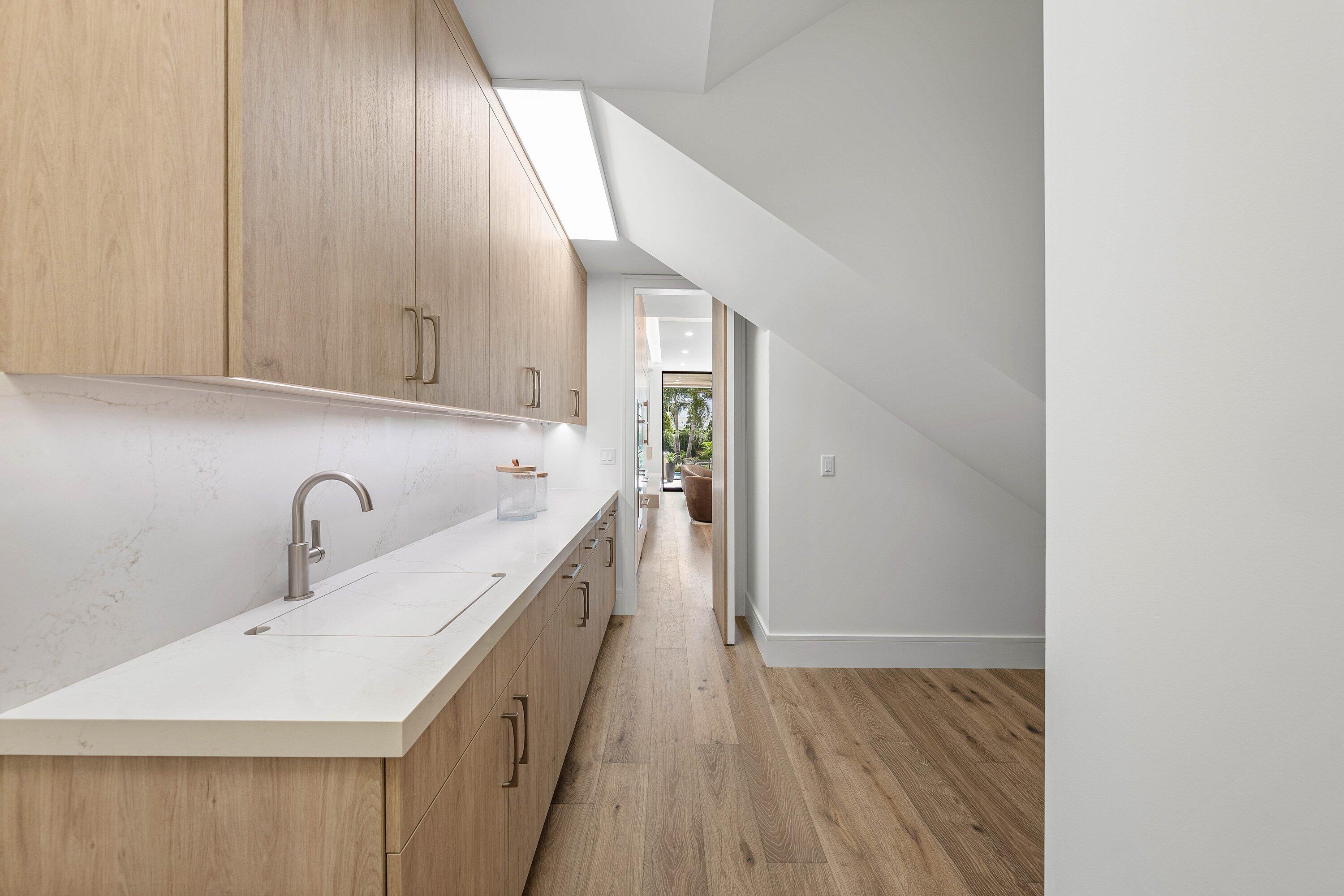 Narrow kitchen with light wood cabinetry, a long white countertop, and a skylight beneath a sloped ceiling.
