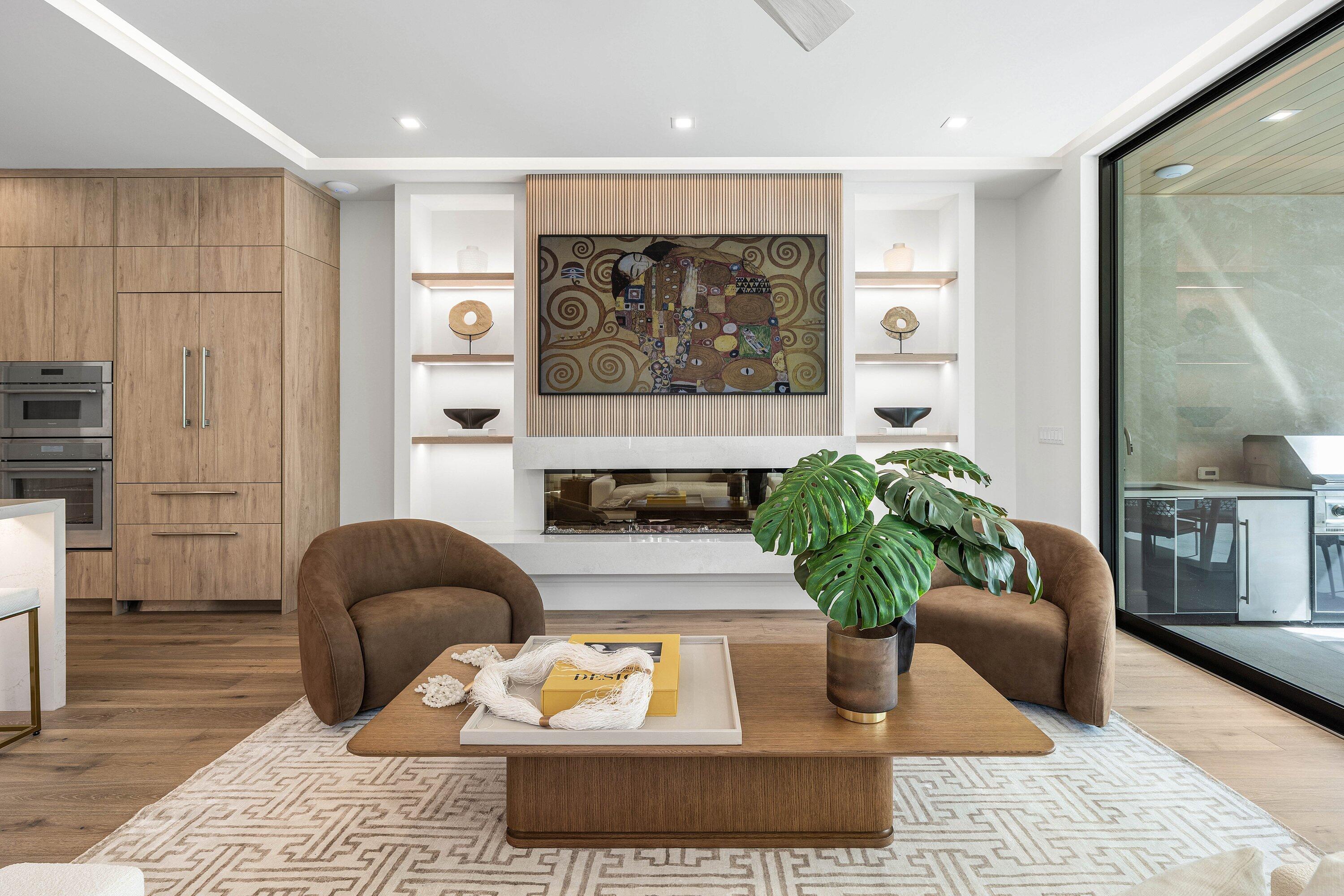Modern living room with a linear fireplace, sculptural brown chairs, and sliding glass doors to an outdoor kitchen.