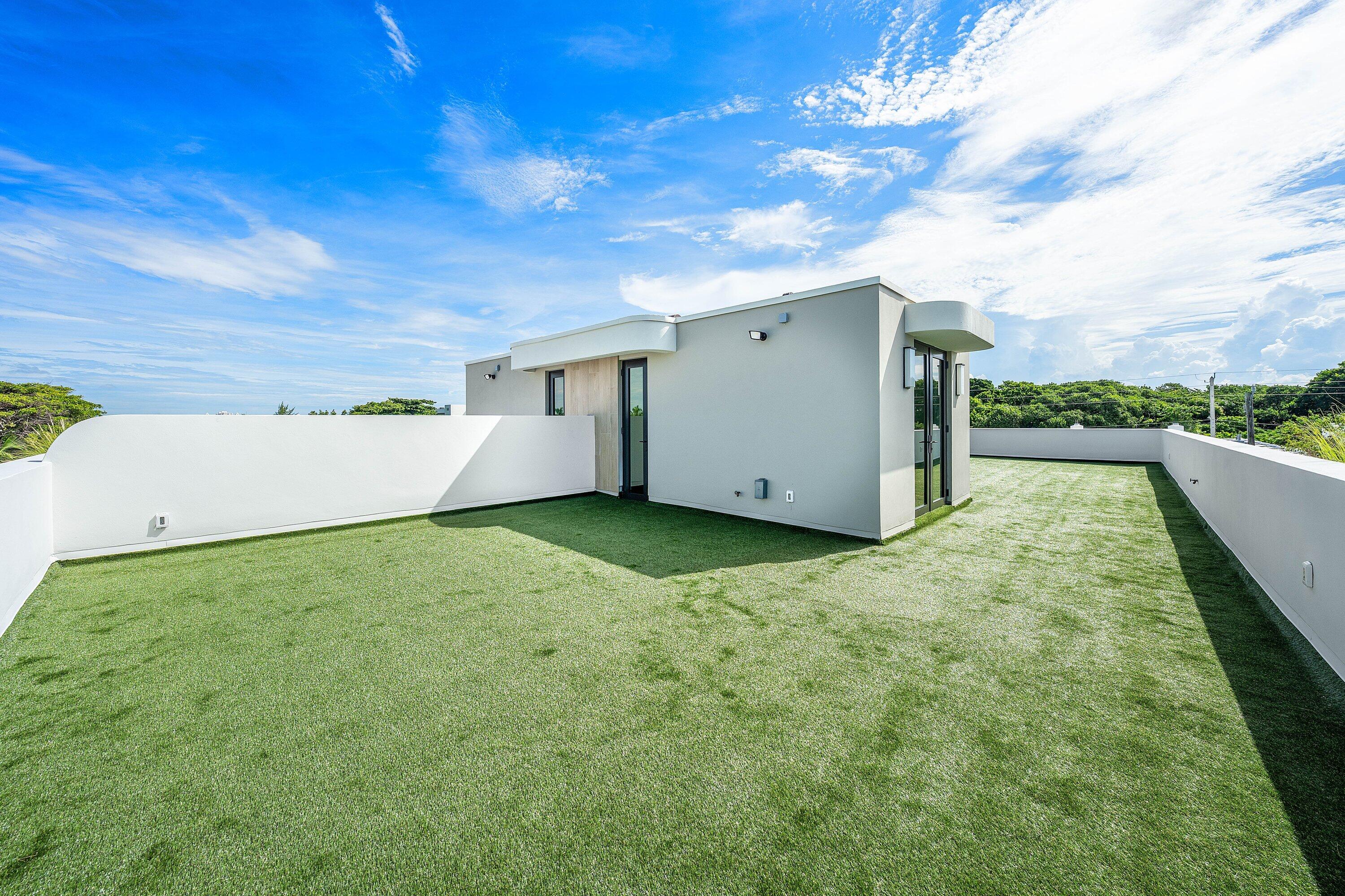 Rooftop terrace with artificial grass, white parapet walls, and a modern rooftop structure.
