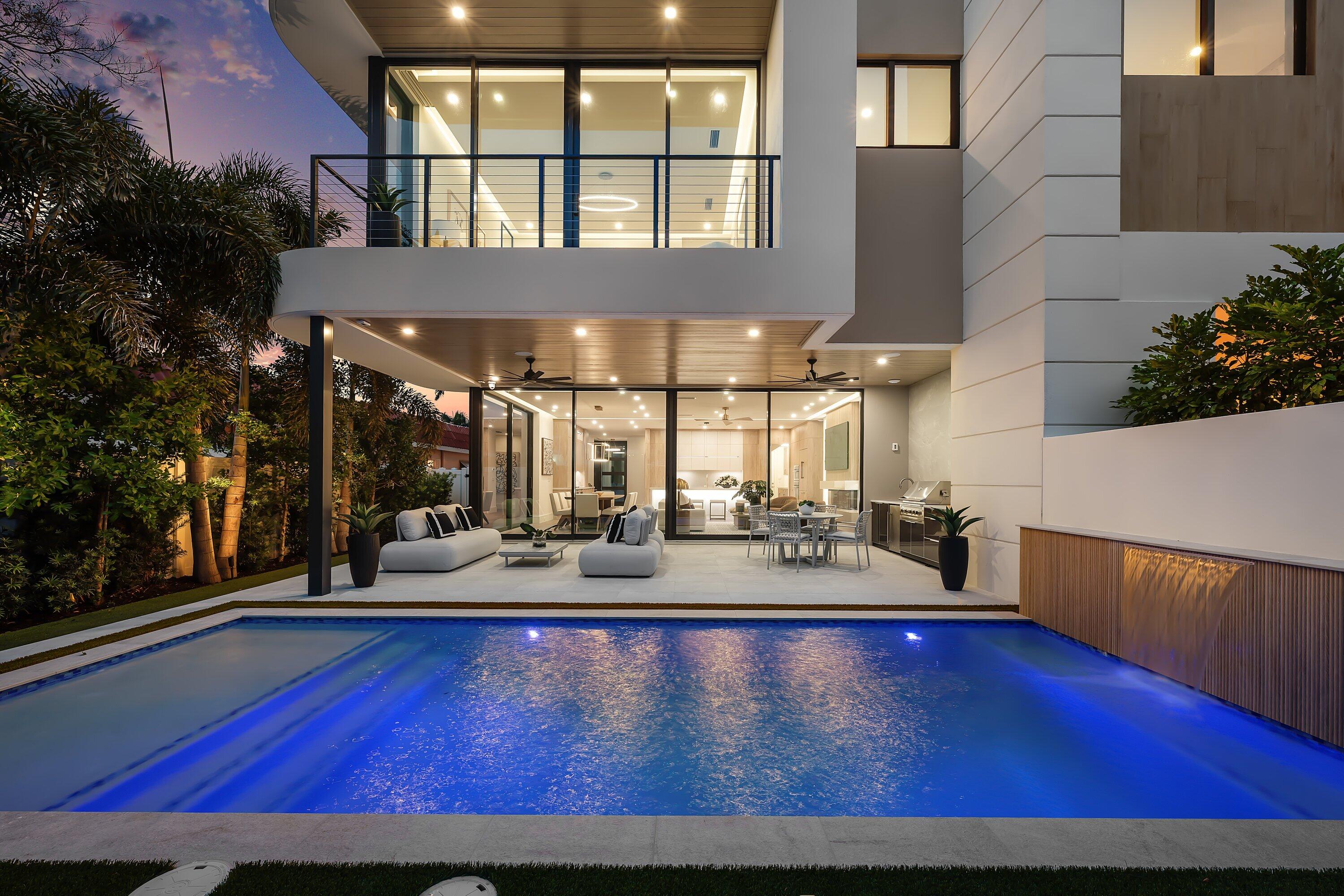 Modern home with an illuminated pool, waterfall feature, and furnished patio at dusk.